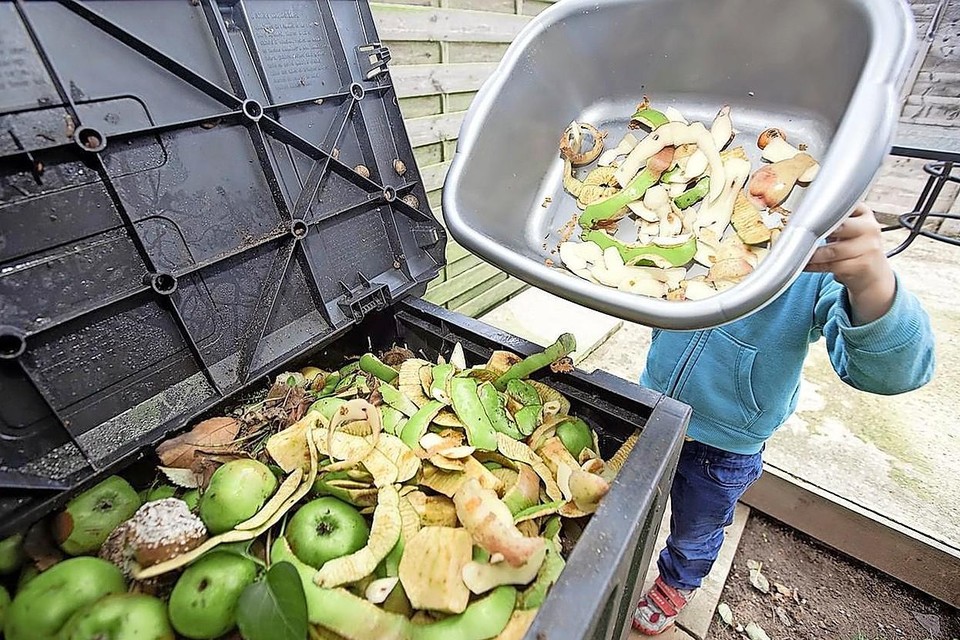 Jonge jongen gooit appelschillen weg in een compostbak