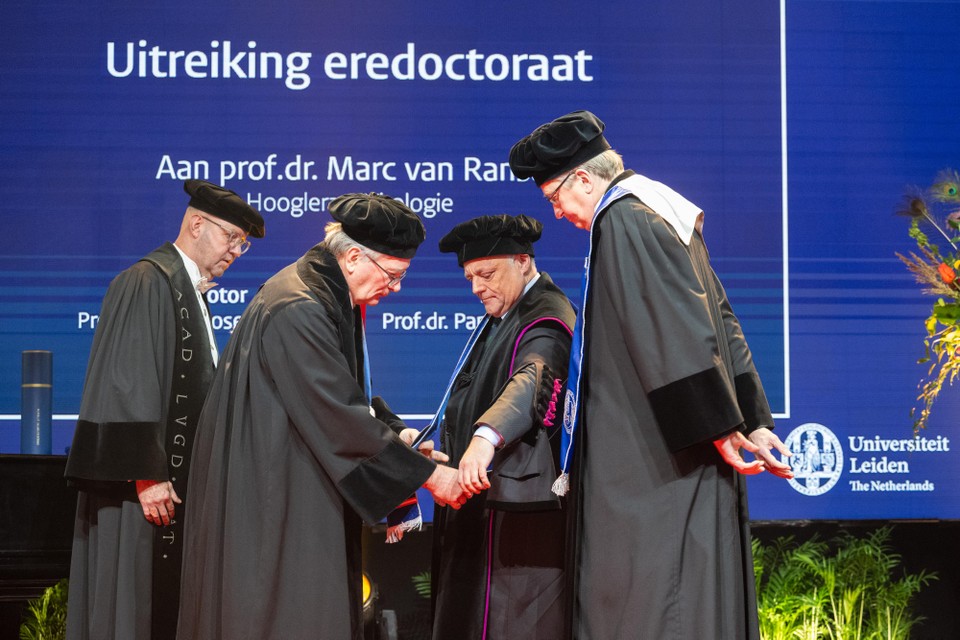 Erepromotor Frits Rosendaal (links) hangt Marc Van Ranst de sjerp om die bij het eredoctoraat hoort. De pedel (uiterst links) en decaan Pancras Hogendoorn (rechts) van de Faculteit Geneeskunde kijken toe.
